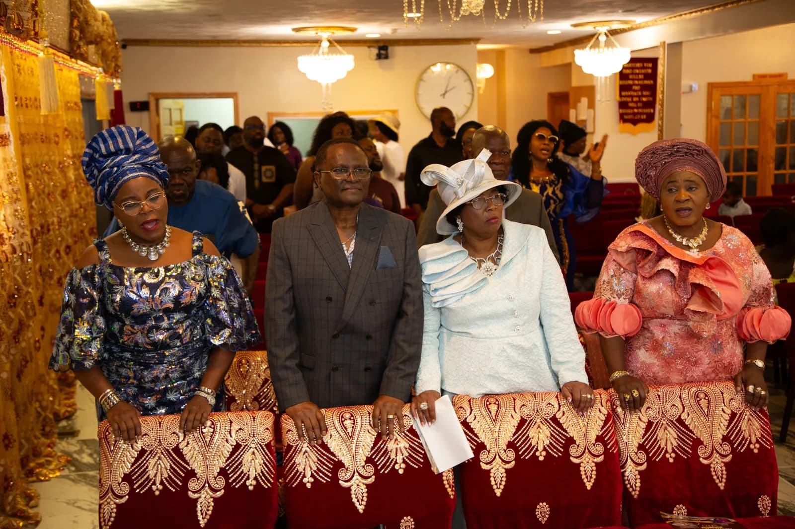 Four elegantly dressed members at their pew — full sanctuary in background