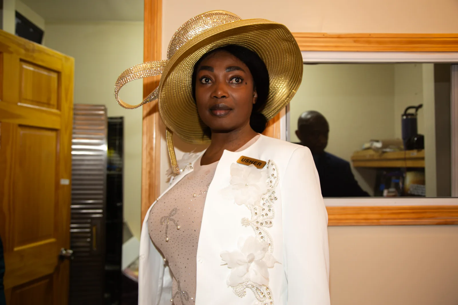Usher in a stunning white gown and broad gold hat — elegant and commanding